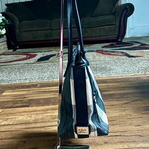 May include: A black and white striped tote bag with a black leather handle and a silver metal stand. The bag has a black leather trim and a small silver tag with the word "Vera" on it.