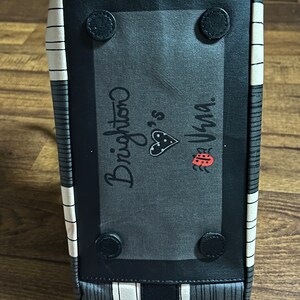May include: Black and white striped tote bag with a black patch featuring the text "Brighton" and a ladybug graphic. The patch has black rivets around the edges.