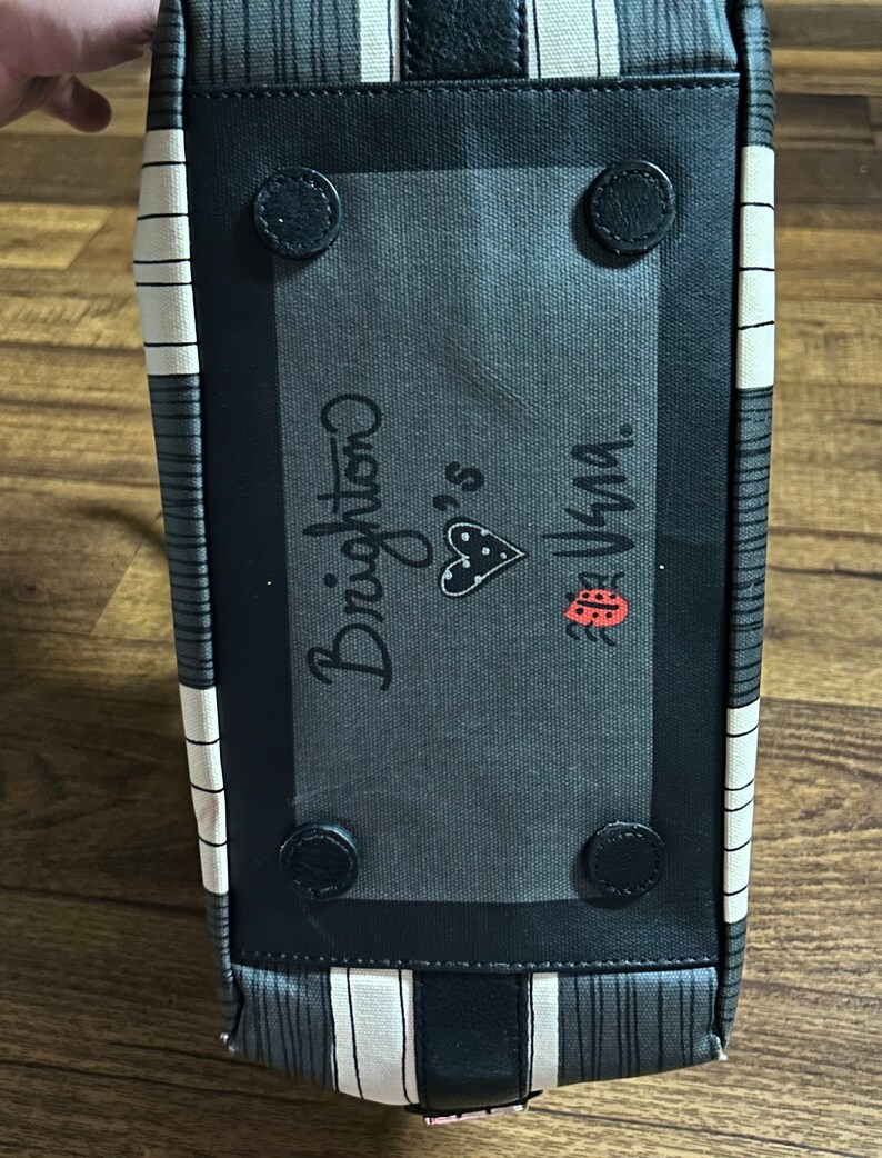 May include: Black and white striped tote bag with a black patch featuring the text "Brighton" and a ladybug graphic. The patch has black rivets around the edges.