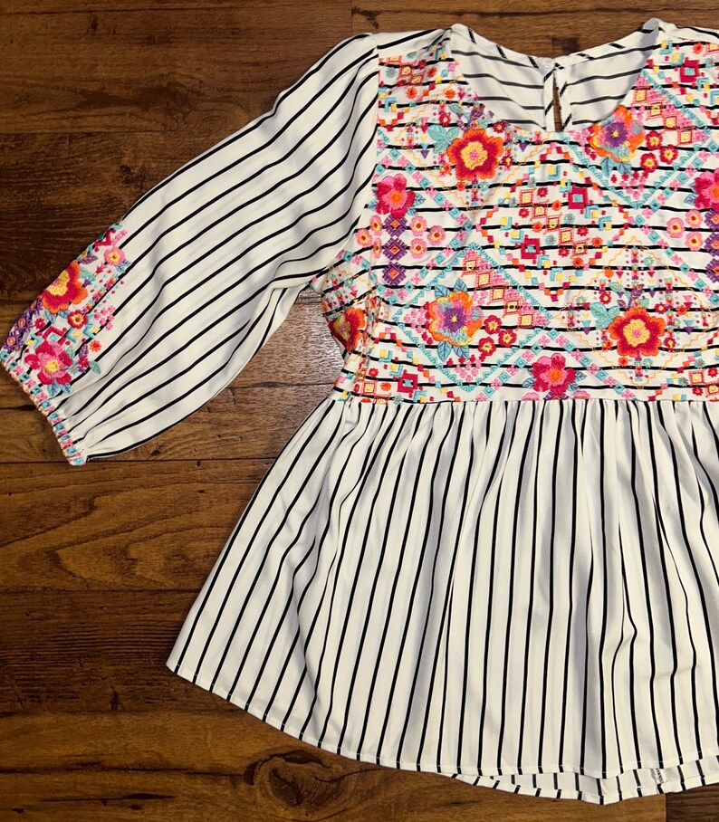 May include: White and black striped blouse with colourful embroidered floral design on the bodice.