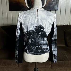 May include: A black and white blazer with a landscape print on the back. The blazer has black sleeves and a classic cut. The landscape print features trees and a cloudy sky.