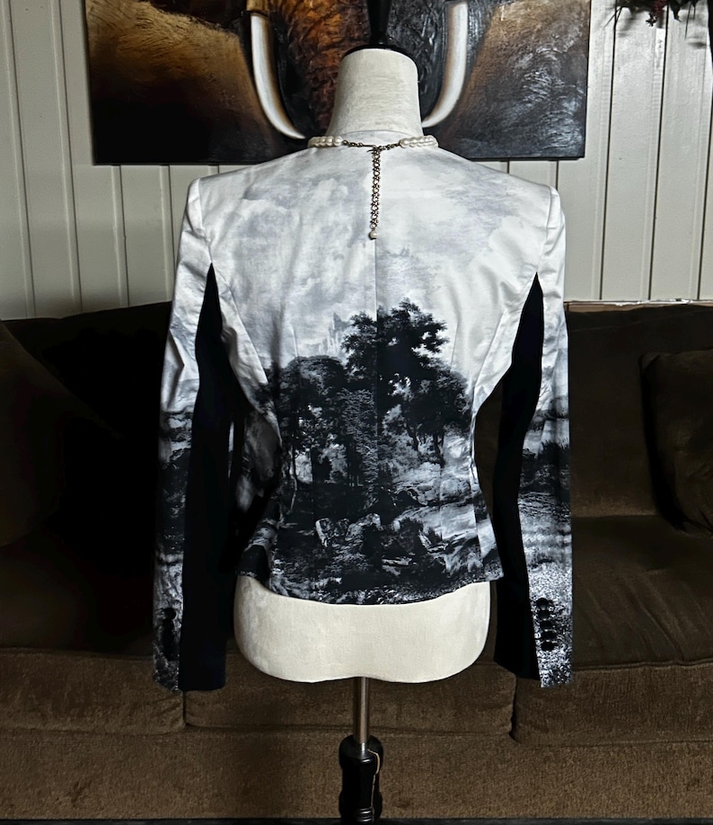 May include: A black and white blazer with a landscape print on the back. The blazer has black sleeves and a classic cut. The landscape print features trees and a cloudy sky.