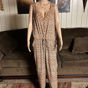 May include: A sleeveless, button-down jumpsuit with a drawstring waist. The jumpsuit is made of a lightweight fabric with a floral pattern in shades of orange, brown, and white.