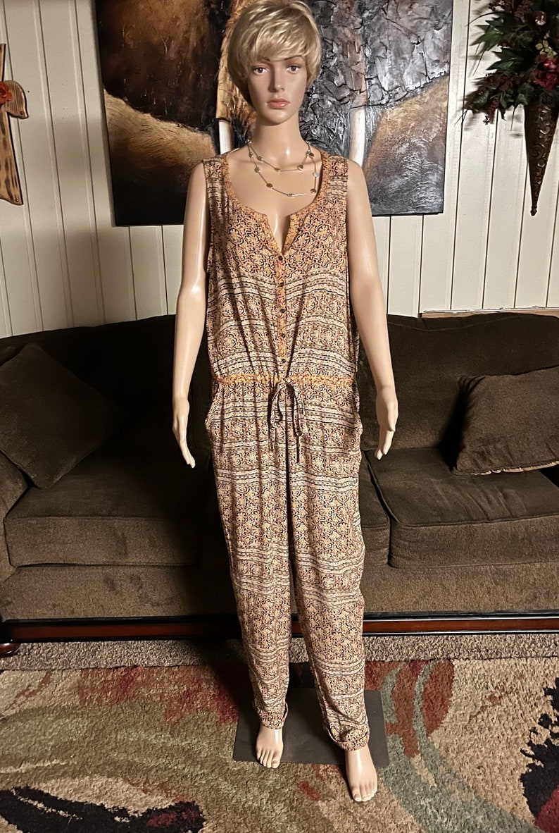May include: A sleeveless, button-down jumpsuit with a drawstring waist. The jumpsuit is made of a lightweight fabric with a floral pattern in shades of orange, brown, and white.