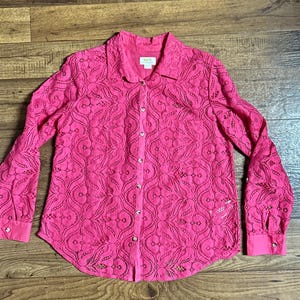 May include: A pink lace button-up shirt with a delicate floral pattern. The shirt has long sleeves and a classic collar.
