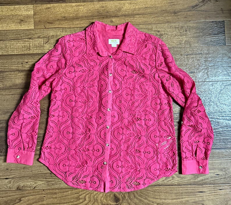 May include: A pink lace button-up shirt with a delicate floral pattern. The shirt has long sleeves and a classic collar.