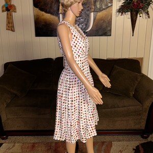 May include: A white, sleeveless dress with a V-neck and a flared skirt. The dress is covered in a pattern of colorful polka dots in shades of red, blue, brown, and pink. The dress is displayed on a mannequin.