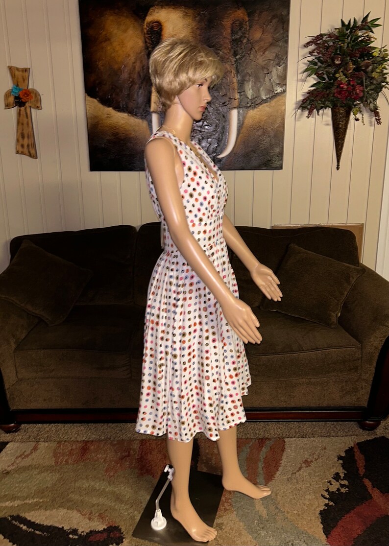 May include: A white, sleeveless dress with a V-neck and a flared skirt. The dress is covered in a pattern of colorful polka dots in shades of red, blue, brown, and pink. The dress is displayed on a mannequin.