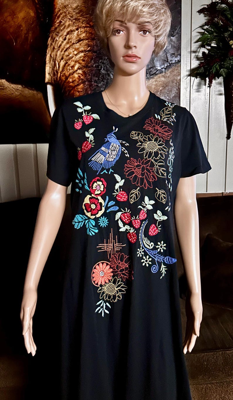 Puede incluir: Una camiseta negra de manga corta con bordados coloridos de un p&aacute;jaro azul, fresas rojas y varios patrones florales. El dise&ntilde;o cubre la parte delantera de la prenda con costuras intrincadas en tonos rojos, azules, amarillos y verdes.