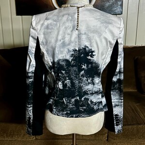May include: A black and white landscape print blazer with black sleeves. The back of the blazer features a detailed monochrome scene of trees and a cloudy sky. The blazer is displayed on a mannequin.