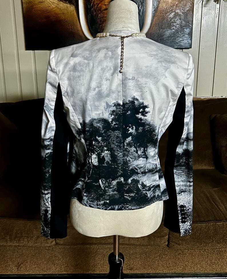 May include: A black and white landscape print blazer with black sleeves. The back of the blazer features a detailed monochrome scene of trees and a cloudy sky. The blazer is displayed on a mannequin.