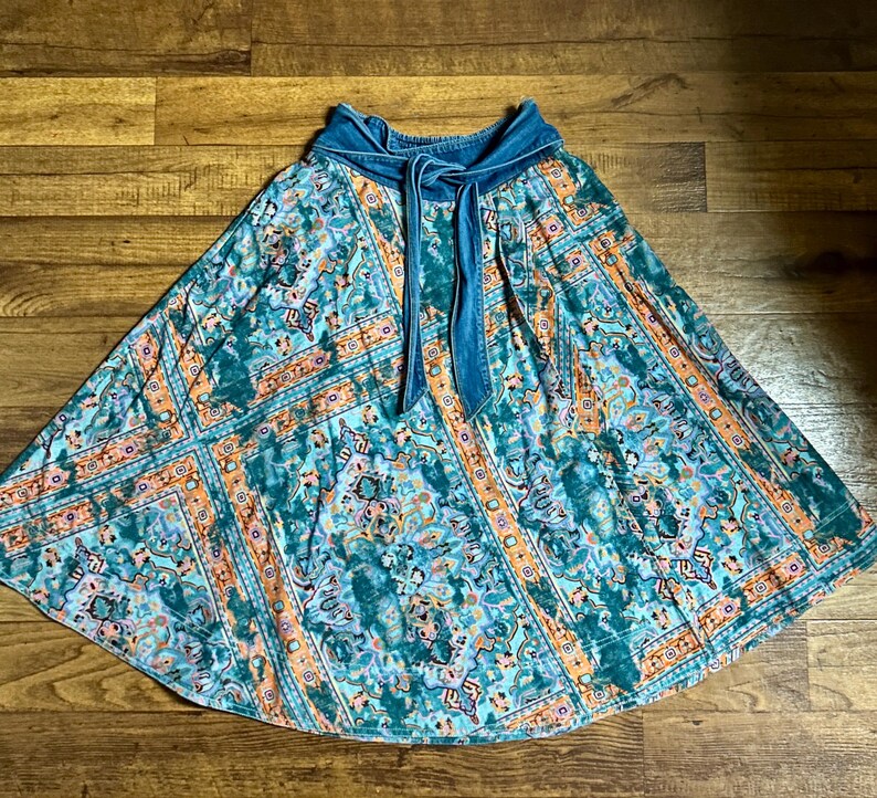 May include: A flowing skirt with a vibrant, patterned design in teal, orange, and purple hues. The skirt features a denim waistband with a tie closure. The fabric has a bohemian aesthetic, suitable for casual wear.