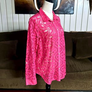 May include: A pink lace button-up shirt with long sleeves. The shirt has a delicate floral pattern and is semi-sheer.
