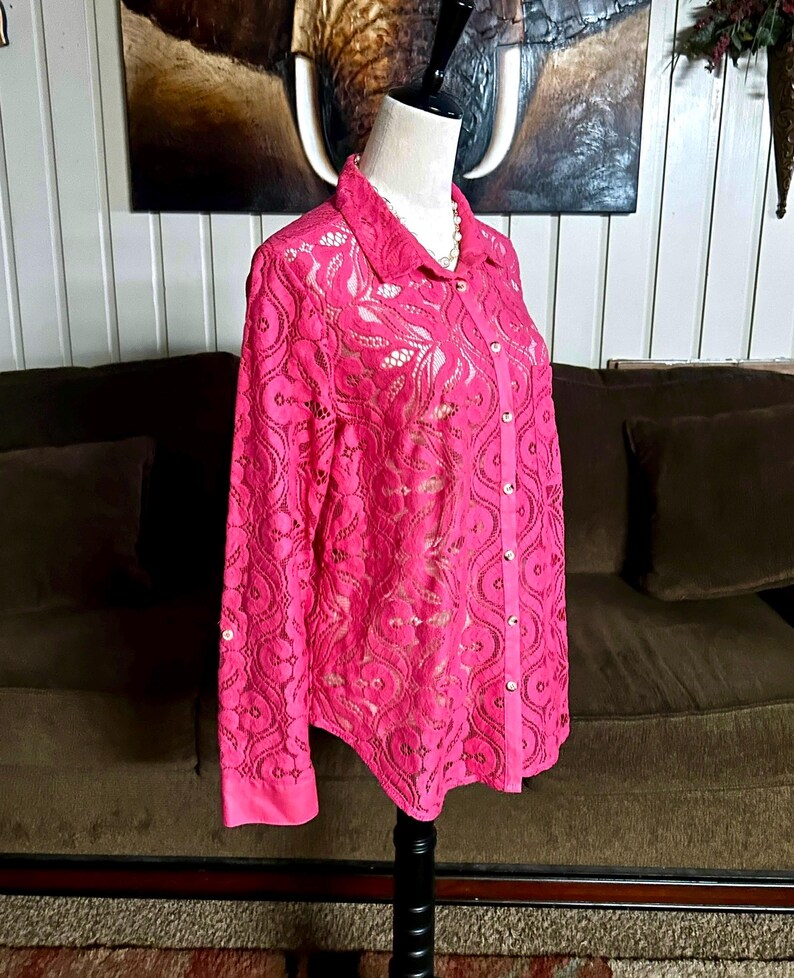 May include: A pink lace button-up shirt with long sleeves. The shirt has a delicate floral pattern and is semi-sheer.