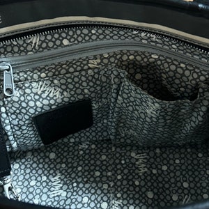 May include: The inside of a black tote bag with a gray and white polka dot lining. The bag has a zippered pocket and a large open pocket.