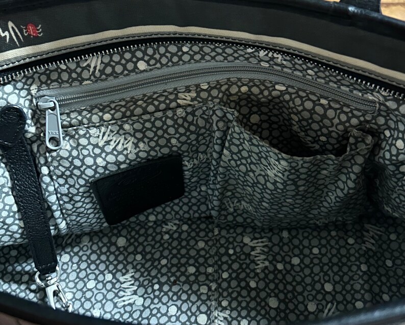 May include: The inside of a black tote bag with a gray and white polka dot lining. The bag has a zippered pocket and a large open pocket.