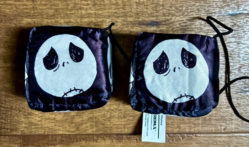 Puede incluir: Dos bolsas de dados en blanco y negro con la cara de Jack Skellington de Pesadilla antes de Navidad. Cada bolsa tiene una cara blanca con ojos negros y una boca cosida. Las bolsas est&aacute;n sobre una superficie de madera.