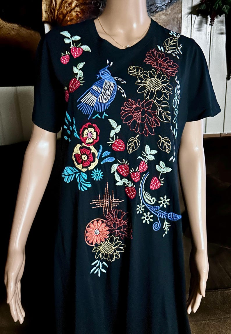 Puede incluir: Una camiseta negra de manga corta con bordados coloridos de un p&aacute;jaro azul, fresas rojas y varias flores en tonos amarillos, rojos y azules. El dise&ntilde;o est&aacute; distribuido por la parte delantera de la prenda, mostrando un detallado trabajo de costura.