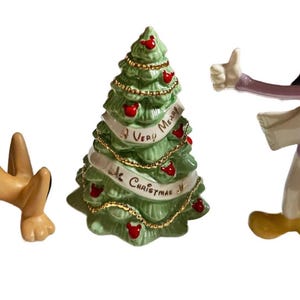 Może przedstawiać: Zestaw świątecznych figurek z postaciami Disneya Pluto i Goofy'ego oraz zieloną ceramiczną choinką. Na choince widnieje napis "A Very Merry Christmas". Figurki są w jasnych kolorach.