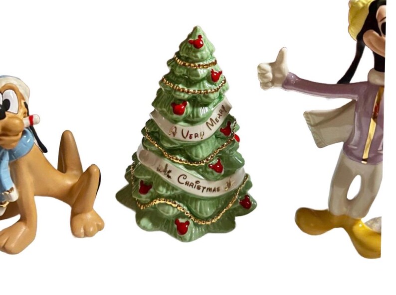 Może przedstawiać: Zestaw świątecznych figurek z postaciami Disneya Pluto i Goofy'ego oraz zieloną ceramiczną choinką. Na choince widnieje napis "A Very Merry Christmas". Figurki są w jasnych kolorach.