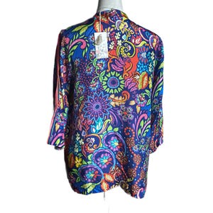 May include: A vibrant, long-sleeved top with a colorful floral pattern in shades of blue, red, purple, and green. The top features a flowing design and a tag attached near the neckline. The overall style is bohemian.