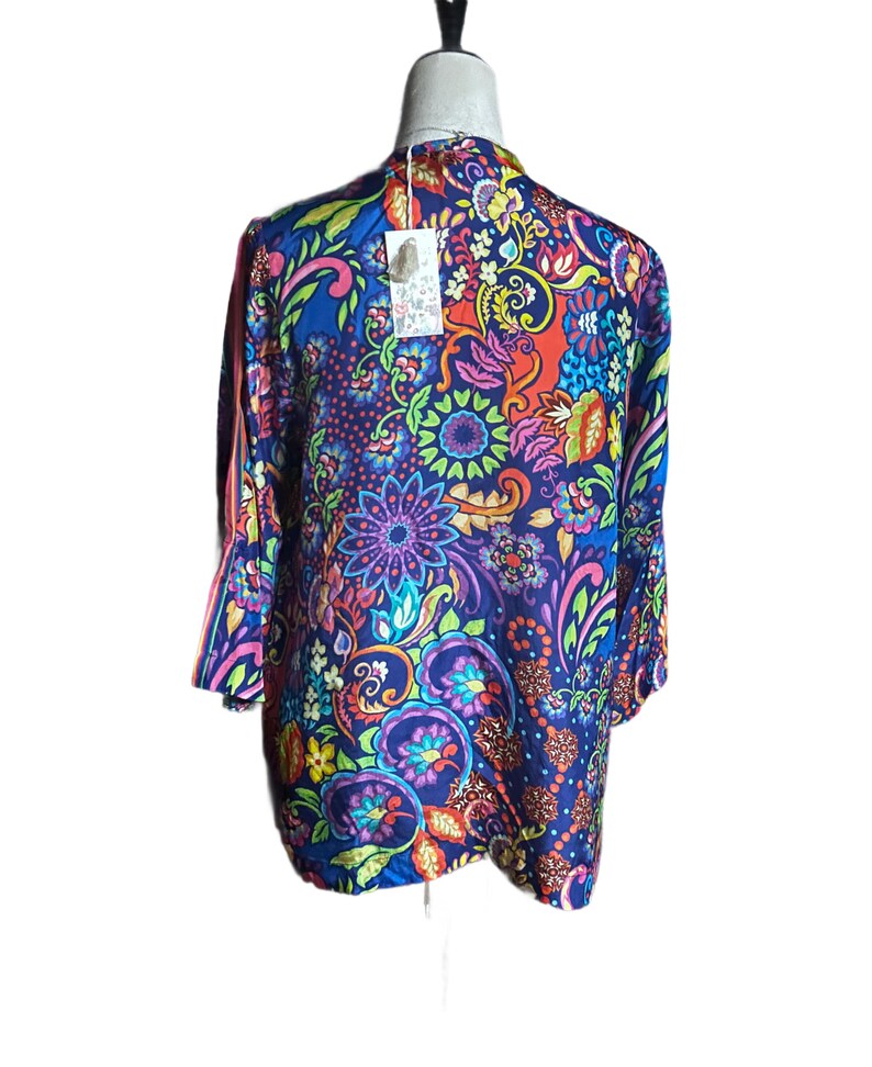 May include: A vibrant, long-sleeved top with a colorful floral pattern in shades of blue, red, purple, and green. The top features a flowing design and a tag attached near the neckline. The overall style is bohemian.