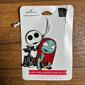 Puede incluir: Adorno navide&ntilde;o Hallmark con Jack Skellington y Sally de The Nightmare Before Christmas. El adorno tiene una cuerda blanca para colgar. El texto "Jack Skellington and Sally" est&aacute; impreso en la parte inferior.
