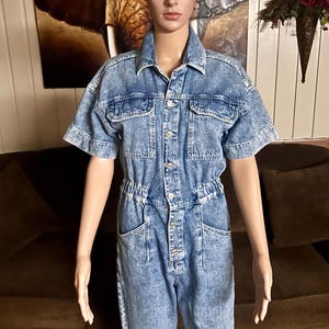 Peut inclure: Une combinaison en jean bleu clair &agrave; manches courtes, avec un devant boutonn&eacute; et plusieurs poches. La combinaison a une taille cintr&eacute;e et une coupe ample.