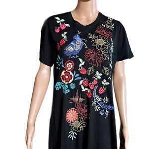 Puede incluir: Una camiseta negra de manga corta con bordados coloridos de un p&aacute;jaro azul, fresas rojas y varios patrones florales en tonos rojo, naranja, amarillo y azul. El dise&ntilde;o se concentra en la parte delantera de la prenda.