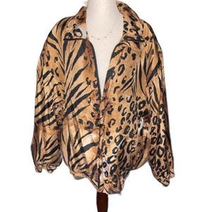 May include: A tan and black animal print jacket with a zipper closure. The jacket features a mix of tiger stripe and leopard spot patterns. The jacket is displayed on a mannequin.