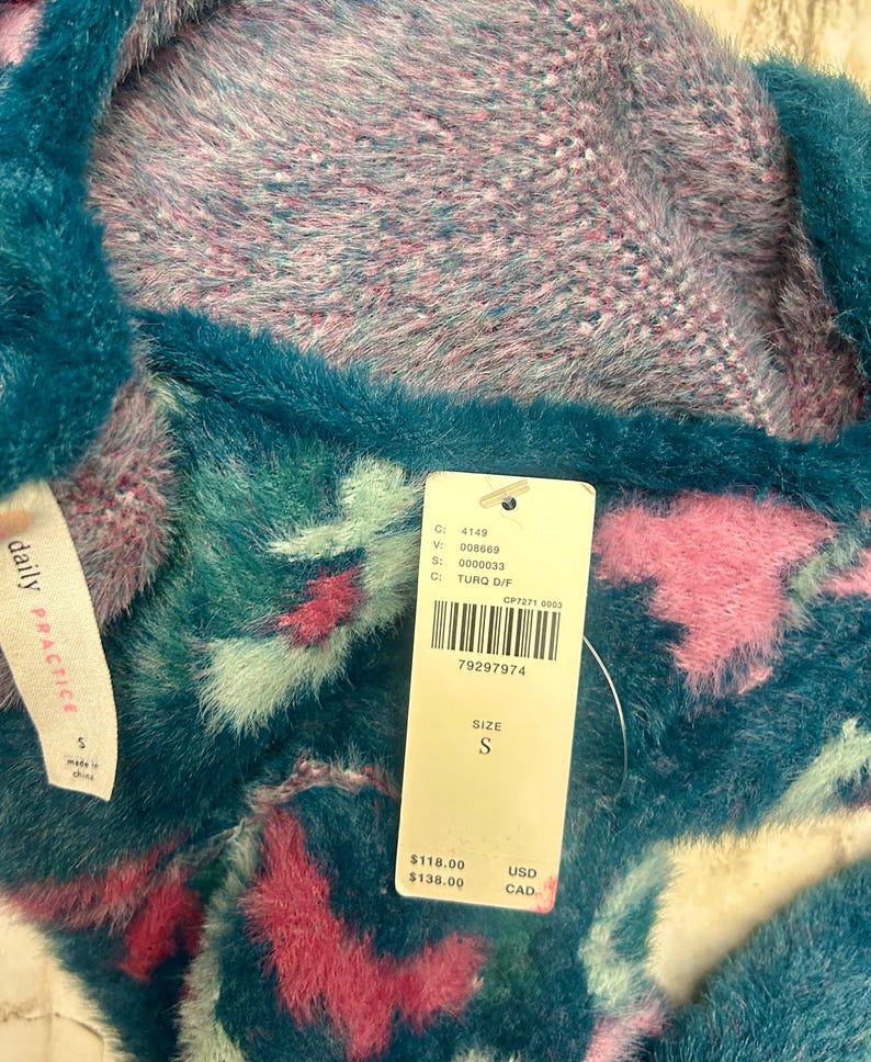 May include: A teal blue and pink fuzzy sweater with a white tag that says "daily PRACTICE" and has the text "C: 4149, V: 008669, S: 0000033, C: TURQ D/F, CP7271 0003, 79297974, SIZE S, $118.00 USD, $138.00 CAD".