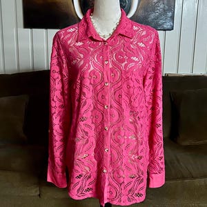 May include: A pink lace button-up shirt with long sleeves. The shirt has a delicate floral pattern.