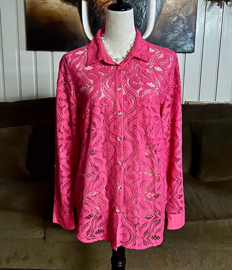 May include: A pink lace button-up shirt with long sleeves. The shirt has a delicate floral pattern.