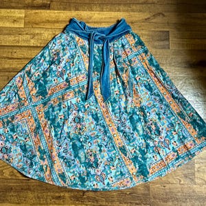 May include: A teal and orange patterned skirt with a denim waistband and tie. The skirt features a floral and geometric design. The skirt is a flowing, A-line style, suitable for casual wear.