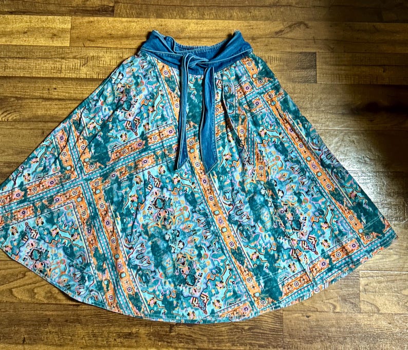 May include: A teal and orange patterned skirt with a denim waistband and tie. The skirt features a floral and geometric design. The skirt is a flowing, A-line style, suitable for casual wear.