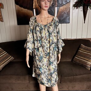 Puede incluir: Un vestido de estampado floral blanco, amarillo y azul con cuello redondo y mangas 3/4. El vestido tiene un dobladillo con volantes y un ajuste holgado.