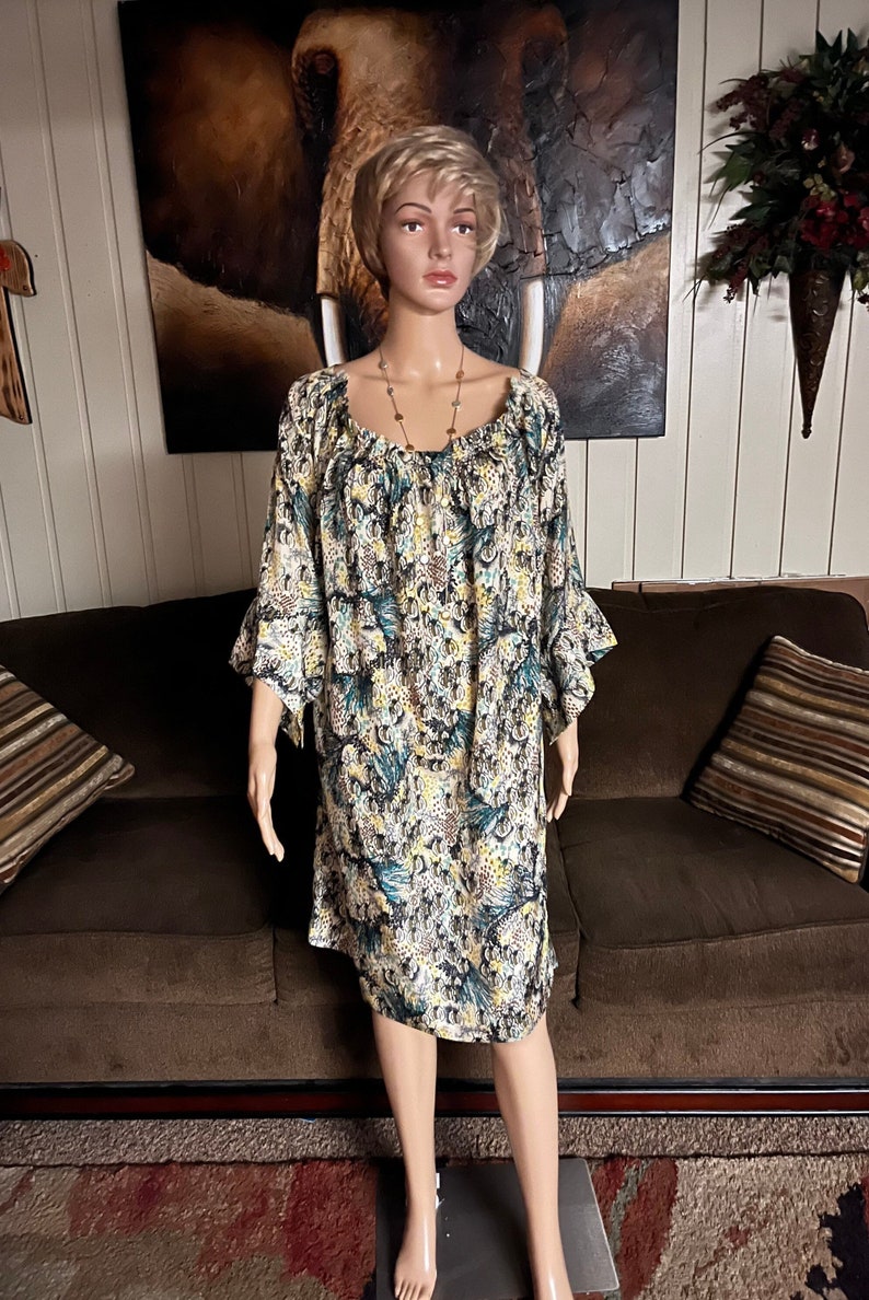Puede incluir: Un vestido de estampado floral blanco, amarillo y azul con cuello redondo y mangas 3/4. El vestido tiene un dobladillo con volantes y un ajuste holgado.