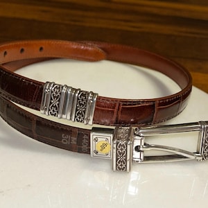 May include: A brown leather belt with a crocodile texture. The belt has a silver buckle and decorative silver accents. The belt is approximately 30 inches in length.