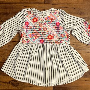 May include: White and black striped blouse with a floral embroidered yoke. The embroidery features pink, red, blue, and yellow flowers.