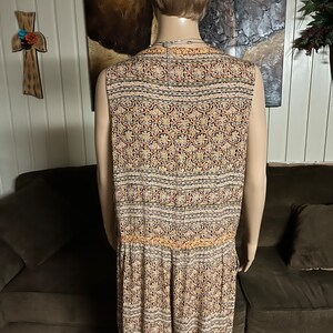May include: A sleeveless jumpsuit with a patterned design in shades of beige, brown, red, and black. The pattern features intricate floral and geometric motifs.