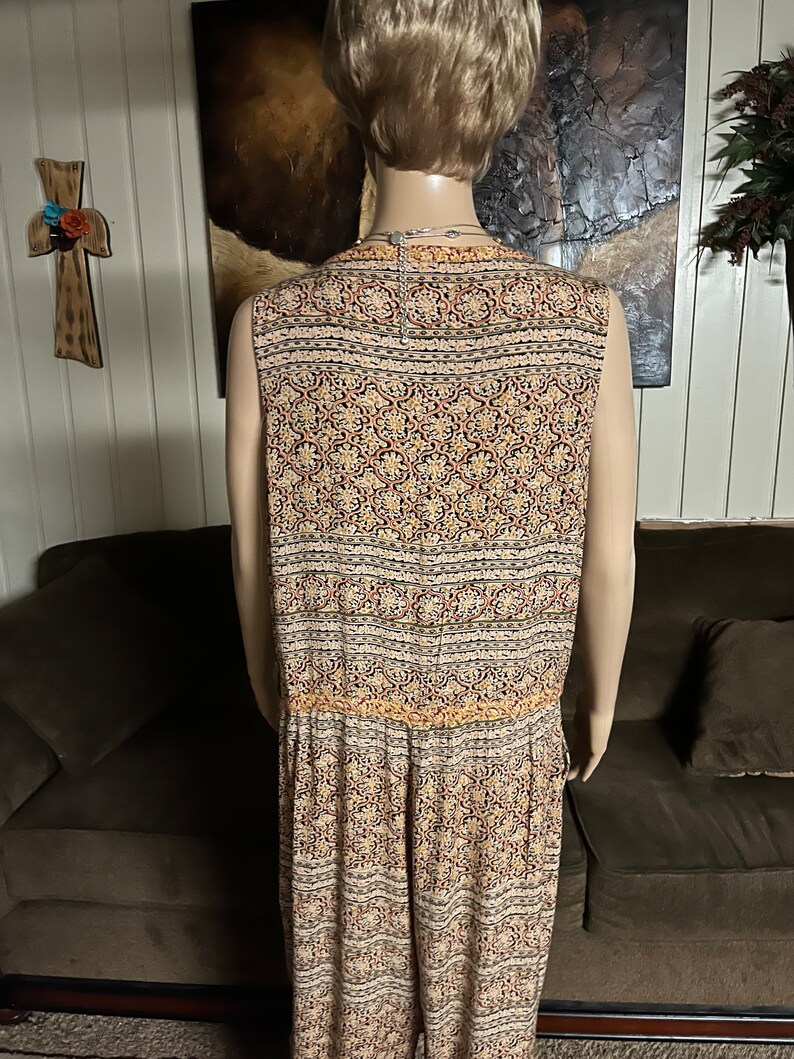 May include: A sleeveless jumpsuit with a patterned design in shades of beige, brown, red, and black. The pattern features intricate floral and geometric motifs.