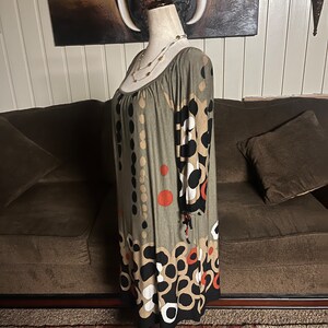 May include: A green, brown, black, and white patterned dress with 3/4 sleeves. The dress has a scoop neck and a loose fit. The dress is on a mannequin.