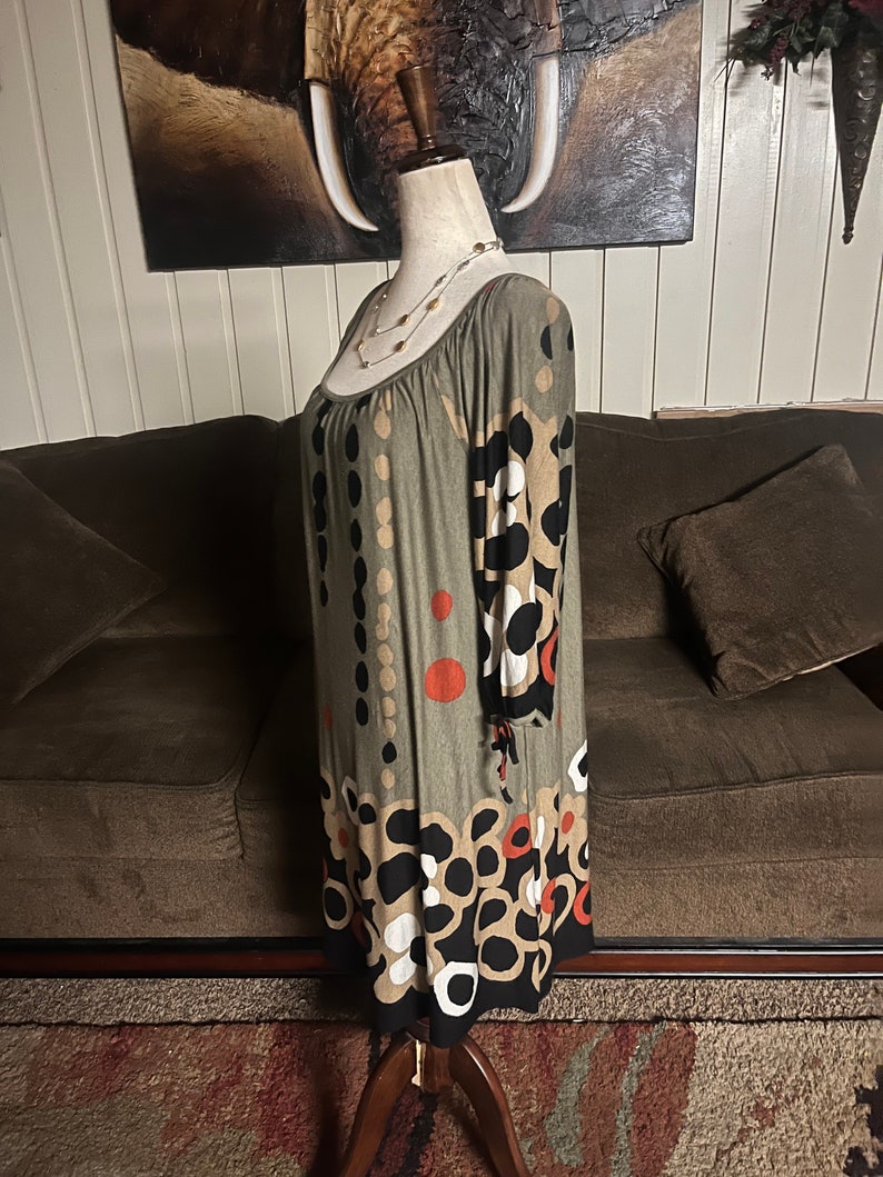 May include: A green, brown, black, and white patterned dress with 3/4 sleeves. The dress has a scoop neck and a loose fit. The dress is on a mannequin.