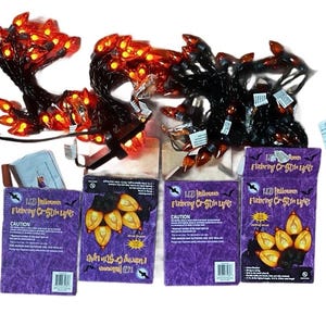 May include: A set of LED Halloween flickering C7 style lights with orange bulbs on black wire, accompanied by four purple cardboard boxes labeled LED Halloween Flickering C7 Style Lights, along with two instruction manuals and a small paper insert.