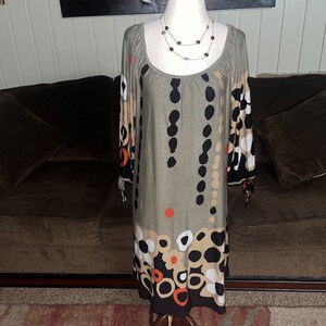 May include: A gray, long-sleeved dress with a scoop neck and a black, white, and orange geometric pattern. The dress has a loose fit and is made of a soft, stretchy fabric.