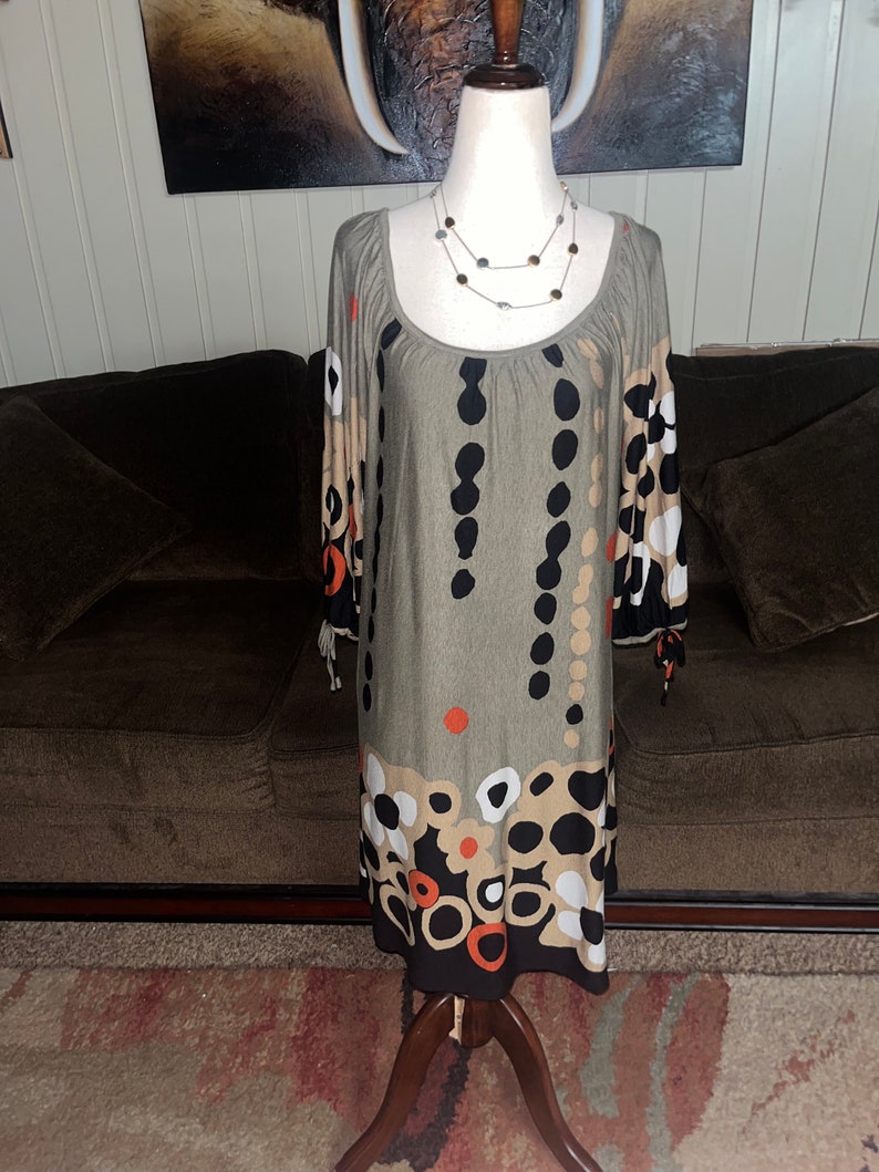 May include: A gray, long-sleeved dress with a scoop neck and a black, white, and orange geometric pattern. The dress has a loose fit and is made of a soft, stretchy fabric.