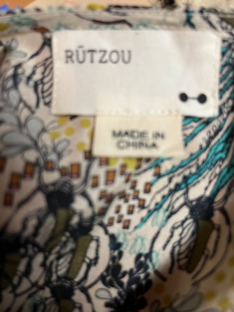 Puede incluir: Una etiqueta blanca con el texto "R&Uuml;TZOU" en letras negras. Debajo del texto hay una etiqueta blanca m&aacute;s peque&ntilde;a con el texto "MADE IN CHINA" en letras negras.