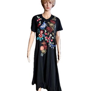 Puede incluir: Un vestido midi negro de manga corta con cuello redondo y dobladillo con volantes. La parte delantera del vestido est&aacute; decorada con bordados coloridos que representan varias flores, hojas verdes, fresas rojas peque&ntilde;as y un p&aacute;jaro azul.