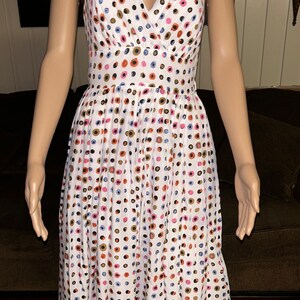 May include: White sleeveless dress with a V-neckline, adorned with a pattern of colorful polka dots in shades of pink, blue, brown, and black. The dress has a fitted bodice and a flared skirt, creating a classic silhouette.