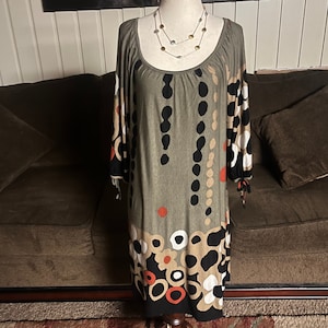 May include: A green, brown, black, white, and red patterned dress with a scoop neck and 3/4 sleeves. The dress is on a mannequin and has a beaded necklace around the neck.